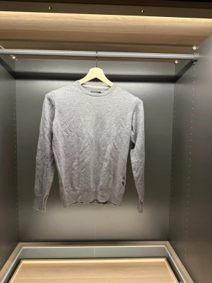 Grå merinoulltröja från Riley - Snygg och stilren grå tröja från Riley i mjuk och tunn merinoull. Klassisk rund halsringning och ribbade muddar vid ärmslut och nederkant. Perfekt för lager-på-lager och funkar året runt. Den är M men sitter som Xs/S för den tvättats fel.