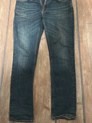 Nudie Jeans blå jeans 34/32 - Säljer ett par klassiska blå jeans från Nudie Jeans i storlek 34/32. Jeansen har snygg slitning, raka ben och kontrastsömmar. Tillverkade i slitstarkt denim med två bakfickor och detaljerad söm på fickorna.