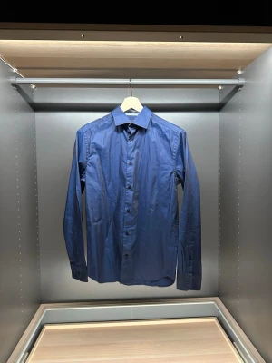 Blå skjorta från Riley Regular Fit - Snygg blå skjorta från Riley i regular fit. Klassisk krage, långa ärmar och knappar framtill. Skjortan är tillverkad i ett mjukt bomullstyg och har en stilren look som passar perfekt till jeans eller chinos.