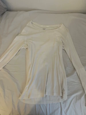 Vit långärmad topp från H&M L.O.G.G. - En enkel och stilren vit långärmad topp från H&M:s L.O.G.G.-kollektion. Toppen har rund halsringning och är gjord i mjuk bomull som känns skön mot huden. Perfekt att matcha med jeans eller kjol för en clean look.
