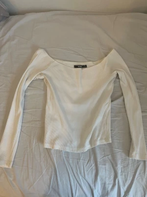 Vit ribbad offshoulder topp Bik Bok - Säljer en vit ribbad offshoulder topp från Bik Bok i storlek S. Toppen har lång ärm och är tillverkad i ett stretchigt material som sitter snyggt på kroppen. Perfekt att styla med jeans eller kjol för en clean look.