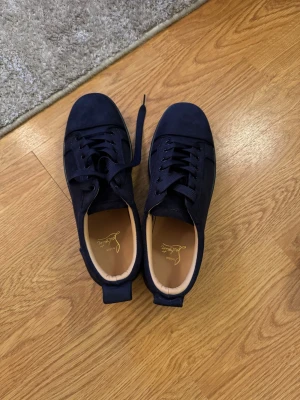 Mörkblå sneakers från Christian Louboutin - Box ingår Helt oanvända 10/10 skick Snygga mörkblå sneakers från Christian Louboutin i mocka med klassisk röd sula och diskret logga på insidan. Skorna har rund tå, svarta snören och en stilren design som passar till det mesta. Insidan är beige och ger en lyxig känsla.