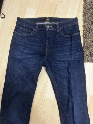 Mörkblå Lee Malone jeans W31 L30 - Säljer ett par mörkblå Lee Malone jeans med klassisk femficksdesign och snygga kontrastsömmar. Jeansen har normal passform och är tillverkade i slitstarkt bomullsmaterial. Perfekta för dig som gillar tidlös denimstil.