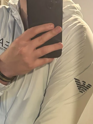 Emporio Armani  - Bilden visar endast ett ljusgrått träningsset från Emporio Armani EA7, bestående av jacka och byxor. 