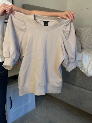 Beige tröja med puffärm från Lindex - Säljer en beige tröja från Lindex med puffiga trekvartsärmar och bred mudd vid ärmslut och nederkant. Tröjan har en rund halsringning och är gjord i mjuk bomull, perfekt för en chill och stilren look.