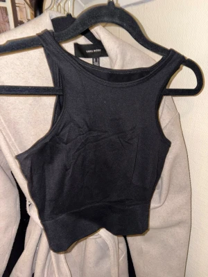 Svart croppad linnetopp Vero Moda - Säljer en svart croppad linnetopp från Vero Moda. Toppen har en hög halsringning och är ärmlös med en tight passform. Tillverkad i mjukt och stretchigt material som sitter snyggt på kroppen. Perfekt att styla med jeans eller kjol.