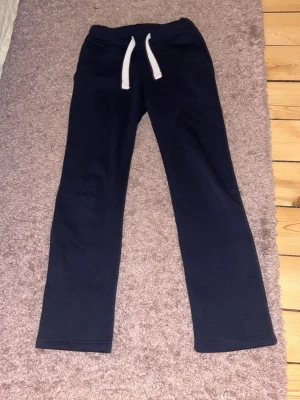 Mörkblå mjukisbyxor XXS med snörning - Mörkblå mjukisbyxor från Russemerch i storlek XXS. Byxorna har vita snören i midjan och raka ben. Tillverkade i mjukt bomullsmaterial, perfekta för chill dagar eller träning. Klassisk och enkel design utan mönster.