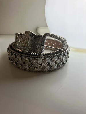 Glittrigt silverbälte med diamanter  - Ett snyggt bälte i silver med massor av diamanter och nitar längs hela bandet. Kvaliteten på bältet är riktigt bra. Spännet är dekorerat med små stenar för extra bling. Perfekt för dig som vill sticka ut och addera lite extra till din outfit.