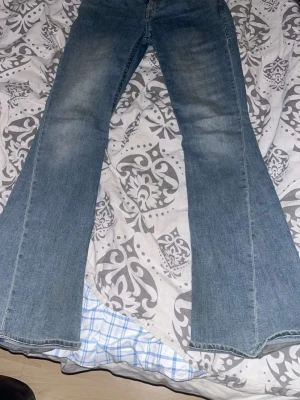 True Religion ljusblå bootcut jeans - Säljer ett par ljusblå bootcut jeans från True Religion med ikonisk bakficka och kontrastsömmar. Jeansen har klassisk femficksdesign och är tillverkade i mjuk bomullsdenim. Perfekta för dig som gillar en retro och avslappnad look. Har hål vid fötterna på båda benen då dom varit lite för långa. Annars i gott skick!