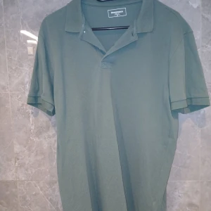 Grön pikétröja från Dressmann - Snygg grön pikétröja från Dressmann i klassisk modell med krage och korta ärmar. Tillverkad i bomull med pikéstruktur som ger en skön känsla. Perfekt för en avslappnad och stilren look.