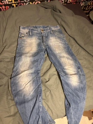 Blå jeans från G-Star RAW - Snygga blå jeans från G-Star RAW med slitna detaljer och ljusa partier framtill och baktill. Klassisk femficksmodell med G-Star-logga på bakfickan. Jeansen har en rak passform och är tillverkade i denim. Storlek 31/32