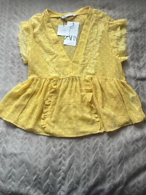 Gul volangblus med spets från Zara - Supersöt gul blus från Zara med volanger och spetsdetaljer. Blusen har v-ringning, korta ärmar med spets och ett prickigt mönster. Perfekt för dig som vill ha en trendig topp till sommaren. Pris kan såklart diskuteras 
