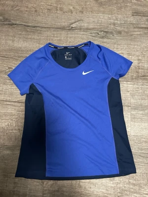 Blå Nike Dri-Fit träningströja - blå träningströja från Nike. Tröjan har korta ärmar, rund halsringning och har lufthål på sidorna och ryggen för extra ventilation. 