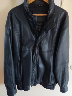 Vintage Svart skinnjacka med dragkedja storlek xl - Klassisk svart skinnjacka med hög krage och dragkedja framtill. Perfekt för dig som vill ha en tidlös och stilren look. Utsida mycket bra skick, insida viss slitage i innertyg mönster, dock helt.