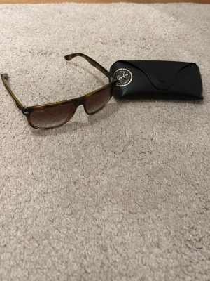 Ray-Ban boyfriend - Snygga solglasögon från Ray-Ban med bruna rektangulära bågar och tonade linser. Bågarna är i plast med sköldpaddsmönster och har diskret Ray-Ban-logga på linsen. Medföljer gör ett svart Ray-Ban-fodral i läderimitation. Har en defekt på en av bågarna då den är lite lös
