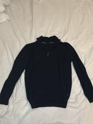 Mörkblå quarter zip från SAND coppenhagen  - En stilren mörkblå tröja med quarterzip och hög krage. Tröjan har långa ärmar och ribbade muddar vid ärmslut och nederkant. Äkta bomull perfekt för lager på lager och enkel att matcha med olika outfits.