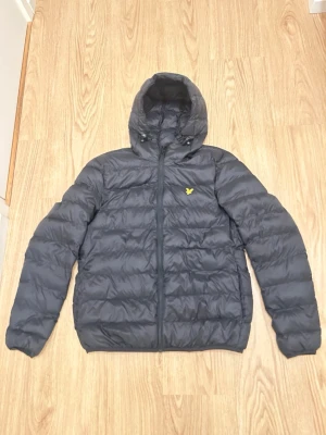 Lyle&Scott Jacka (Perfekt till våren) - NYPRIS: 1000kr   Snygg svart dunjacka från Lyle & Scott med huva och dragkedja framtill. Jackan har det klassiska gula logomärket på bröstet och quiltad design som ger en modern look. Perfekt för kalla dagar och enkel att matcha med olika outfits. OBS: Det står Medium på den men känns lite mindre.