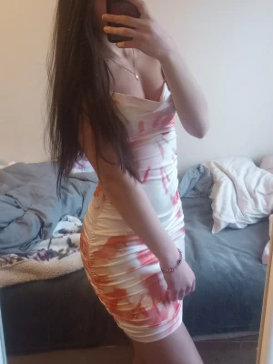 Vit och orange kort klänning - Säljer en snygg kort klänning i vitt med orange mönster. Klänningen är figurnära med omlottliknande överdel och tunna axelband. Perfekt för dig som vill sticka ut med en färgglad och trendig look. Storlek XS/S! Aldrig använd, endast testad! 