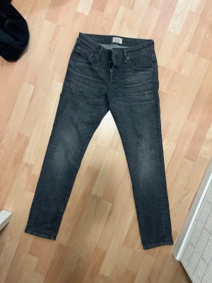 Mörkgrå skinny jeans från Jack and Jones - Snygga mörkgrå skinny jeans från Jack and Jones med klassisk femficksdesign och knappgylf. Jeansen har en smal passform och är tillverkade i mjukt denimtyg som sitter skönt hela dagen. 29W 32L