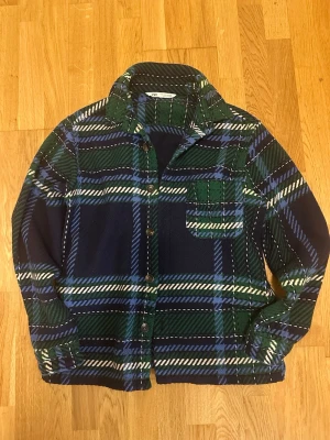 Rutig overshirt från Zara i blått och grönt - Snygg rutig overshirt från Zara i blått, grönt och vitt. Overshirten har klassisk krage, knappstängning framtill och en bröstficka. Perfekt lager-på-lager-plagg med lång ärm och avslappnad passform. Tillverkad i mjukt material som känns skönt mot huden.