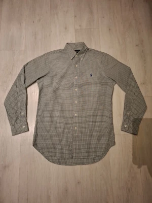 Rutig skjorta från Ralph Lauren - Klassisk rutig skjorta från Ralph Lauren med button-down krage och lång ärm. Skjortan har små rutor i beige, blått och grönt samt den ikoniska broderade loggan på bröstet. Perfekt till jeans eller chinos för en clean och tidlös look. Priset går självklart att diskutera 🙂