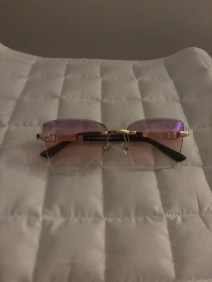 Dolce & Gabbana lila solglasögon - Säljer ett par stilrena solglasögon från Dolce & Gabbana med rektangulära, lila tonade glas och guldfärgade detaljer. Skalmarna är svarta och glasen är utan båge nertill för en modern look. Perfekta för dig som vill sticka ut med en exklusiv accessoar. Perfekta för sommaren o våren