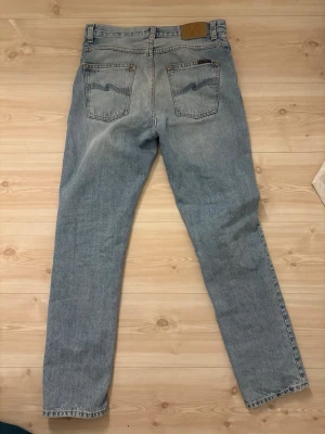 Nudie jeans - Klassiska ljusblå Nudie jeans i rak modell. Jeansen har fem fickor, knappgylf och den ikoniska läderpatchen bak i midjan. Tillverkade i slitstark bomullsdenim med en tidlös look som passar till det mesta. Storleken är W28 L32. Pris går att diskutera.