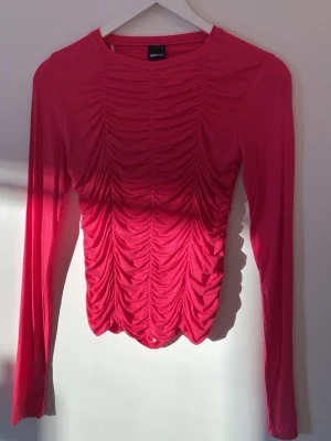 Rosa långärmad topp från Ginatricot - Trendig rosa långärmad topp från Ginatricot med snygg rynkad effekt framtill och baktill. Toppen har en kroppsnära passform och är tillverkad i ett mjukt, stretchigt material som känns bekvämt mot huden. Använd endast 2 gånger.