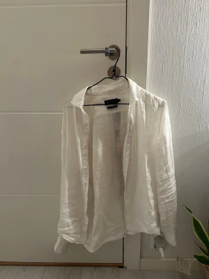 Vit linneskjorta  - Klassisk vit skjorta i luftigt linne. Skjortan har lång ärm, krage och knappar framtill. Perfekt för en avslappnad och stilren look. Passar till både jeans och shorts.