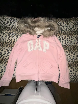 Fur zip up hoodie - Säljer en ljusrosa hoodie från GAP med dragkedja och stor huva kantad med mjuk fuskpäls. Den har få små fläckar som knappast syns som var där när jag köpte den. Efter jag köpte den använde jag den aldrig så jag säljer vidare den. Storlek 13 år men passar mig som är XS-S, kan passa mindre
