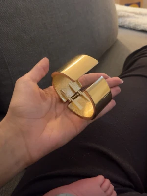 Guldigt chunky armband - Säljer ett chunky armband i metall med guldfärgad finish. Armbandet har en bred, böjd form och öppnas med ett gångjärn i mitten. Perfekt statement piece för dig som gillar att sticka ut med accessoarerna.