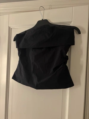 Svart off shoulder topp med dragkedja - Trendig svart off shoulder topp med dragkedja i ryggen. Sitter snyggt och har en lätt figurnära passform. Perfekt att styla med jeans eller kjol för en cool look.