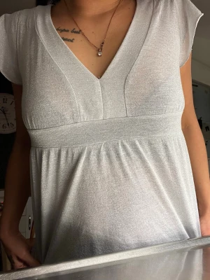 Vit glittrig v-ringad topp - Säljer en vit glittrig topp med v-ringning och korta ärmar. Toppen har en markerad midja och ett lätt, luftigt fall. Perfekt för dig som vill ha något stilrent men ändå med lite extra shine.