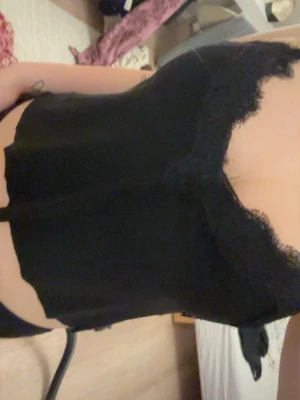 Svart spetslinnetopp - Säljer en svart linnetopp med spetsdetaljer längs urringningen och tunna axelband. Toppen har en enkel och stilren design som passar perfekt till många olika outfits. Men har klippt av den då den var för lång 