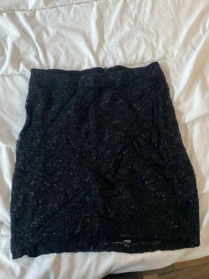 Svart spetskjol med dragkedja - Säljer en svart kortkjol med spetsdetaljer och dragkedja bak. Kjolen har en figurnära passform och är perfekt för dig som gillar en stilren men ändå lite festlig look. Materialet känns mjukt och följsamt.