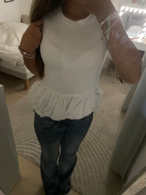 Vit volangtopp med ärmlös design - Supersöt vit topp med volang nertill och ärmlös design. Rund halsringning och figurnära passform som ger en fräsch och trendig look. Perfekt att matcha med jeans eller kjol för en stilren outfit. Toppen är jätte snygg till våren men också för middagar med familj eller kompisar. Jag köpte den i sommmras men jag har inte andvänd den/eller tvättat ( det är bara pris lappen som jag drog bort eftersom jag trodde den skulle komma till andvöndnig ) kontakta om frågor,innan köp och för fler bilder ❤️