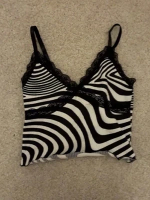 Zebramönstrad croppad linnetopp - Säljer en croppad zebramönstrad linnetopp med svarta spetsdetaljer längs v-ringningen och under bysten. Toppen har smala axelband och är perfekt för dig som gillar statement-plagg och coola mönster.