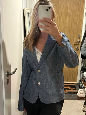Blå kavaj med knappar - Snygg blå kavaj med två knappar framtill och klassisk krage. Kavajen har en lätt strukturerad yta och raka fickor på sidorna. Perfekt för att lyfta vilken outfit som helst med en stilren touch.