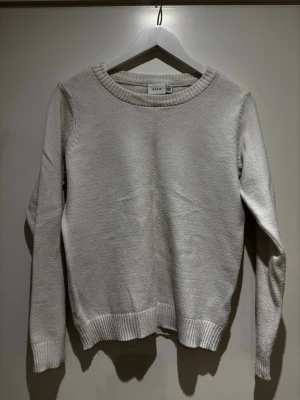 Vit stickad tröja från Vila - Klassisk vit stickad tröja från Vila med rund halsringning och ribbade muddar vid ärmslut och nederkant. Tröjan har en rak passform och är tillverkad i ett mjukt material .