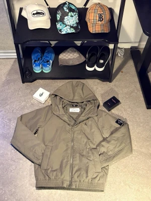 Olivgrön vindjacka från Calvin Klein - Snygg olivgrön vindjacka från Calvin Klein med huva och dragkedja framtill. Jackan har elastisk nederkant och muddar, samt en diskret CK-logga på bröstet och patch på ärmen. Perfekt för vår och höst när du vill ha en lätt och stilren jacka.