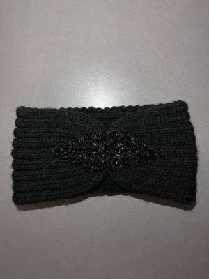 Svart stickat pannband med pärldetalj - Svart stickat pannband med ribbad struktur och en snygg pärlprydd detalj framtill. Pannbandet har en omlottliknande design i mitten vilket gör den mycket smickrande på. Den ät gjord i mjukt stickat material som känns skönt mot huden. Passar huvudstorlek S. Mycket bra skick, som ny! Säljs på flera sidor, först till kvarn. 