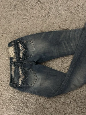 Miss Me bootcut jeans med paljettdetaljer - Säljer ett par Miss Me jeans i bootcut-modell med snygga slitningar och broderade bakfickor med paljetter och silvriga detaljer. jeansen sitter bra och är lågmidjade. orginalpris på jeansen är 1300 kr!💗
