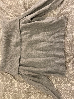 Grå offshoulder stickad tröja - Grå stickad tröja med bred ribbad kant som går över axlarna i offshoulder-stil. Tröjan har lång ärm och loose passform.