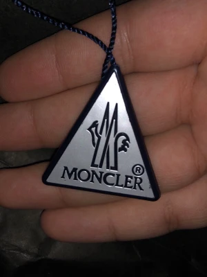 Moncler maya  - Säljer en svart Moncler Maya dunjacka med glansig finish och klassisk logotyp på ärmen. Jackan har rundade dragkedjor med Moncler-emblem och certifierad dunfyllning enligt DIST. Perfekt för dig som vill ha en snygg och varm jacka med exklusiv känsla.