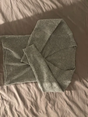 Grå ribbad stickad omlottkofta - Säljer en grå ribbad stickad kofta med omlottdetalj framtill. Koftan har långärmade ärmar och är gjord i ett mjukt stickat material som känns skönt mot huden. Perfekt för lager-på-lager och chill dagar. Snygg twist framtill som gör den extra intressant.