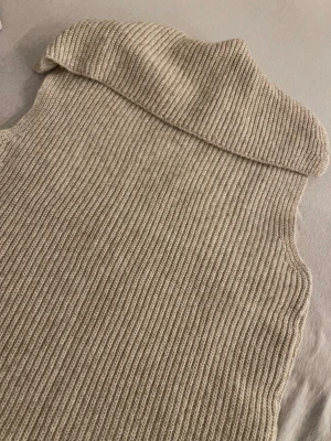 Beige stickad väst med polokrage - Säljer en beige stickad väst från CROPP i storlek S. Västen har en bred polokrage och är ribbstickad över hela plagget. Perfekt att styla över en långärmad tröja för en chill och trendig look.