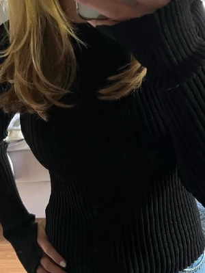 Svart ribbad stickad tröja/glittrig - Säljer en svart, ribbad stickad tröja med lång ärm och rund hals. Tröjan har en slim passform och är gjord i ett mjukt stickat material som sitter snyggt på kroppen. Perfekt att styla med jeans eller kjol för en clean look.