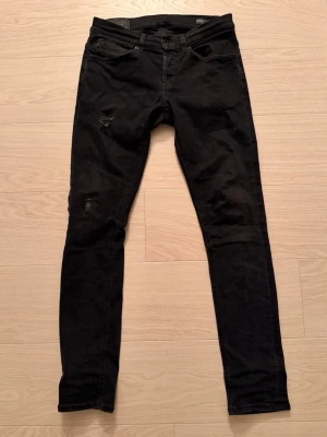 Svarta Jeans från Dondup  - Svarta jeans från dondup med modelen George i skinny fit med klassisk femficksdesign. Byxorna har slitna detaljer på låret och knät för en cool look. Materialet är jeans och passformen är tight. Perfekt för dig som gillar en smal siluett och svart stil.