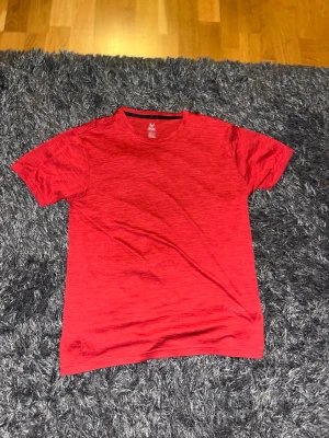 Röd teknisk t-shirt från SOC - Säljer en röd t-shirt från SOC i storlek L, perfekt för träning. T-shirten har korta ärmar och är gjord i ett tekniskt syntetmaterial med TCS Airflow som håller dig torr och bekväm. Enkel design med diskret mönster och rund hals.