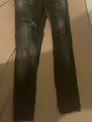 Svarta ripped jeans från Dsquared2 - Säljer ett par svarta jeans från Dsquared2 med snygga slitningar och hål på benen för en edgy look. Jeansen har smal passform och klassisk femficksdesign. Materialet är jeans och färgen är mörk svart. Perfekt för dig som gillar streetstyle. Båda säljs för 500 var, st 42 på dem första och 48 på dem andra 